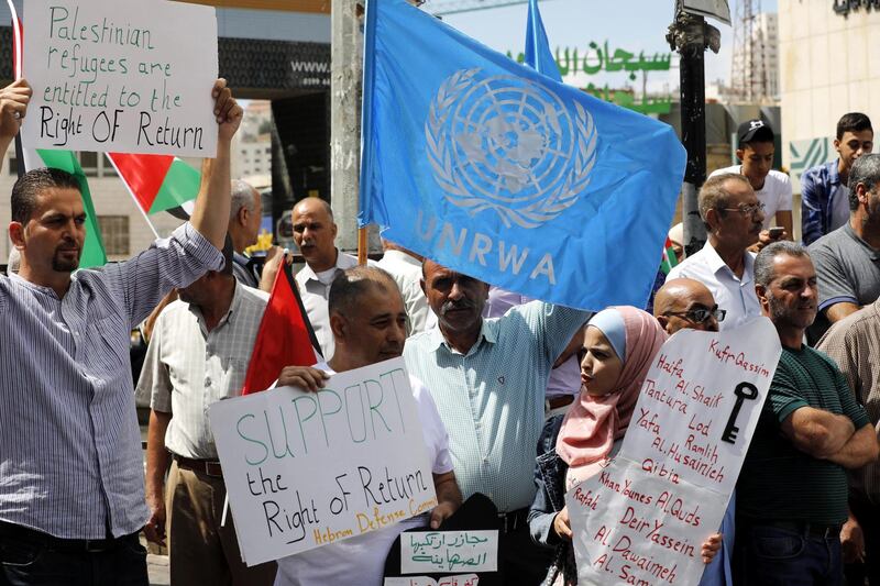 Palestinians hold placards alongside the UN and the Palestinian flags during a protest against US funding cuts for UNRWA in the West Bank city of Hebron. EPA