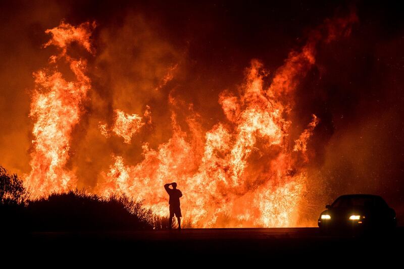 A motorists on Highway 101 watches flames from the Thomas fire leap above the roadway north of Ventura, Calif., on Wednesday, Dec. 6, 2017.  As many as five fires have closed highways, schools and museums, shut down production of TV series and cast a hazardous haze over the region. About 200,000 people were under evacuation orders. No deaths and only a few injuries were reported. (AP Photo/Noah Berger)