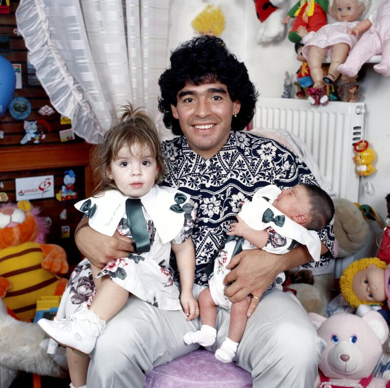 Argentinian football player Diego Armando Maradona sitting in a small bedroom with his daughters Dalma e Giannina in his arms. Italy, 1989 (Photo by Rino Petrosino/Mondadori via Getty Images)