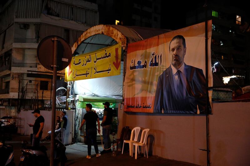 Supporters of Lebanese Prime Minister Saad Hariri stand next of his portrait with Arabic words that read, "God with you," in Beirut, Lebanon. AP Photo