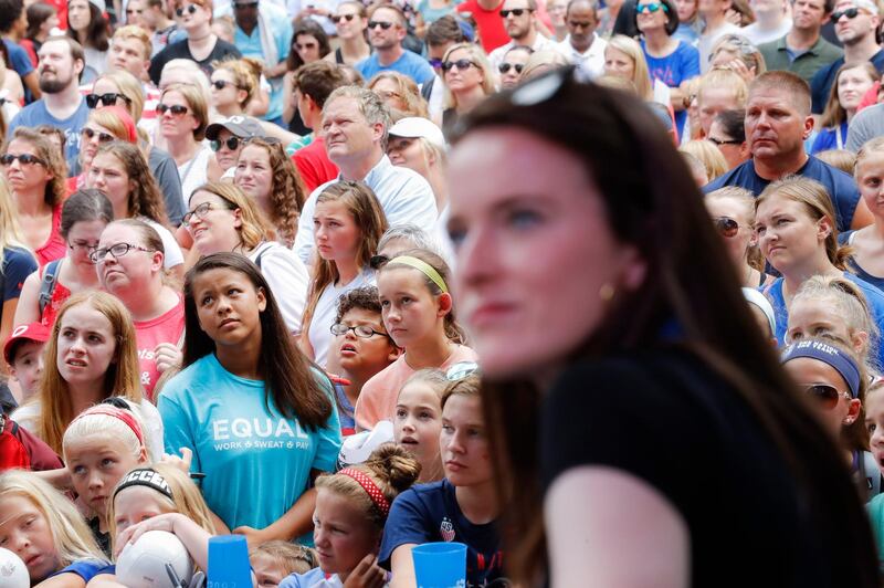 A supporter of U.S. women's soccer team player Rose Lavelle, right foreground, wears an "EQUAL WORK SWEAT PAY" t-shirt during a welcome event in Lavelle's honor at Fountain Square, Friday, July 19, 2019, in Cincinnati. The U.S. national team beat the Netherlands 2-0 to capture a record fourth Women's World Cup title. Lavelle scored the second goal for the U.S. in the victory. (AP Photo/John Minchillo)
