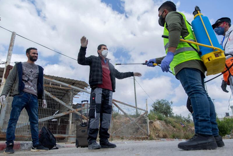 A paramedic from the Palestinian Ministry of Health disinfects Palestinian laborers to help contain the coronavirus, as they exit an Israeli army checkpoint after returning from work in Israel, near the West Bank village of Nilin, west of Ramallah. AP Photo