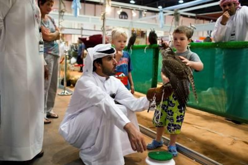 25/09/10 - Abu Dhabi, UAE - Kaelab Scott-Mackie, 4, pets a falcon as Ateeg Al Mazrooe, a captain in the Abu Dhabi Police, bottom left, looks to buy it at the Abu Dhabi International Hunting and Equestrian Exhibition 2010 at ADNEC on Saturday September 25, 2010.(Andrew Henderson / The National)