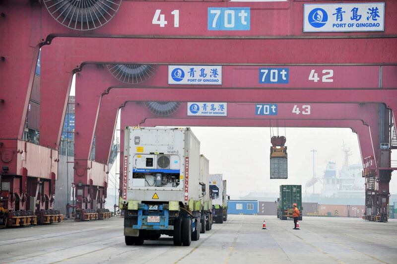 In this Nov. 8, 2017 photo, a worker watches as cargo trucks move through a shipping port in Qingdao in eastern China's Shandong province. China reports its trade growth cooled in December 2017 in a sign of weaker global and domestic demand, but total exports for 2017 rose 7.9 percent over 2016 while imports were up 15.9 percent. (Chinatopix via AP)