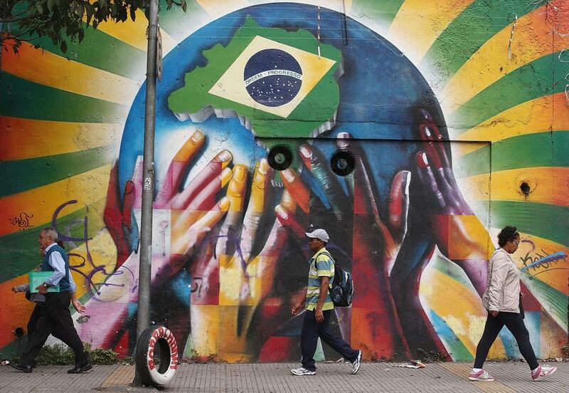 People pass graffiti of multi-coloured hands supporting the planet marked with a Brazilian flag on June 10, 2014 in Sao Paulo, Brazil. Mario Tama / Getty Images