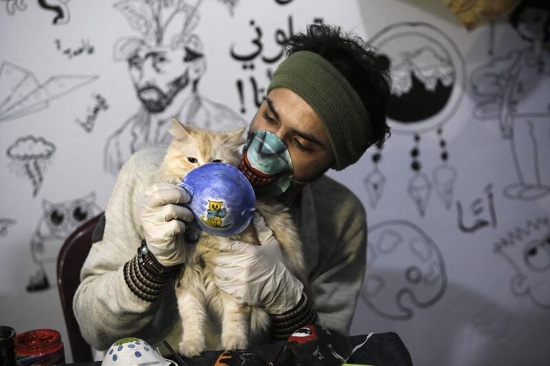 Palestinian artist Dorgham Krakeh holds before a cat a painted dust mask, for a project raising awareness about the COVID-19 coronavirus pandemic, in Gaza City.   AFP