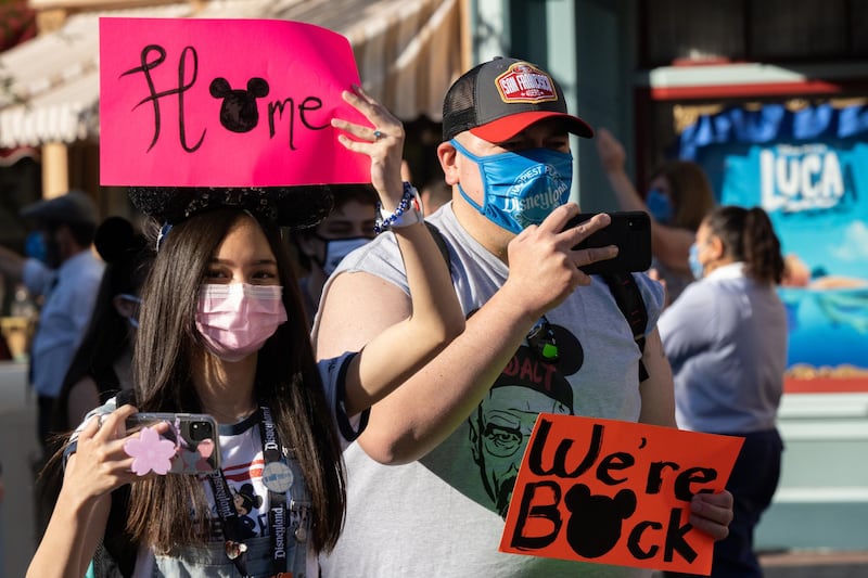 Returning guests wearing protective masks hold up signs on Main Street USA during the reopening of the Disneyland theme park in Anaheim, California, U.S., on Friday, April 29, 2021. Walt Disney Co.'s original Disneyland resort in California is sold out for weekends through May, an indication of pent-up demand for leisure activities as the pandemic eases in the nation's most-populous state. Photographer: Bing Guan/Bloomberg