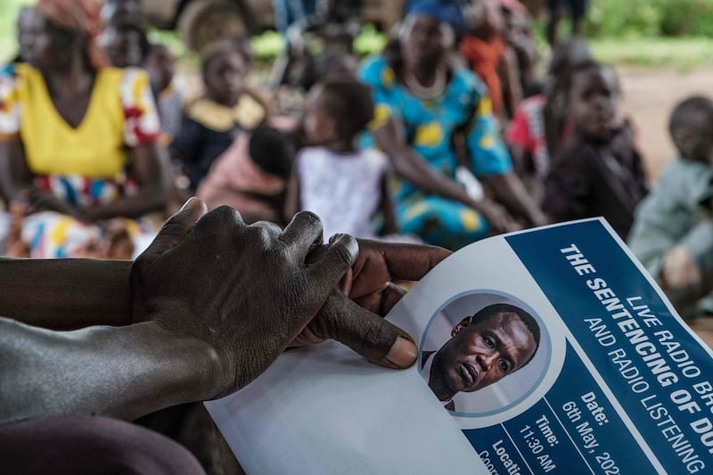A member of Dominic Ongwen's extended family holds a poster as they listen to the sentencing on a radio in Coorom, Ongwen's home village, Uganda, on May 6, 2021. The International Criminal Court on May 6, 2021 sentenced Dominic Ongwen, a Ugandan child soldier who became a commander of the notorious Lord's Resistance Army (LRA), to 25 years in jail for war crimes and crimes against humanity. Ongwen, 45 was found guilty in February 2021 of 61 charges, including murders, rapes and sexual enslavement during a reign of terror in the early 2000s by the LRA, led by the fugitive Joseph Kony. / AFP / Sumy SADURNI

