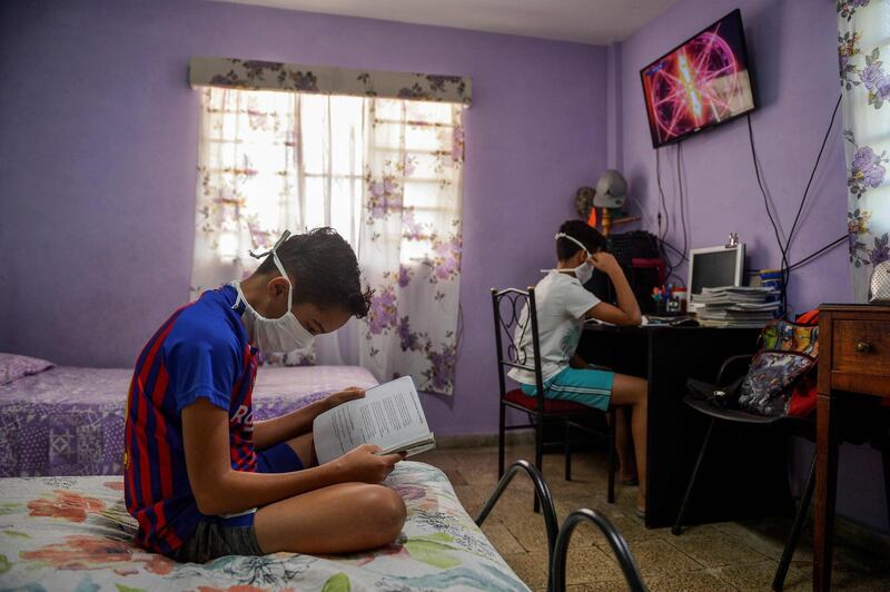 A child watches a class on TV as another reads a book at their home in Havana, on April 23, 2020.  All schools were closed in Cuba due to the COVID-19 pandemic, something unprecedented in 60 years, not even when the strongest hurricanes hit the island. But Cubans had an ace under the sleeve: the teleclass. / AFP / YAMIL LAGE
