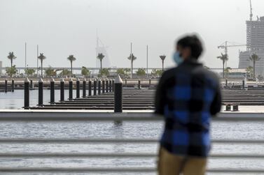 A man looks out over the water with a face mask on during a hazy day in Dubai. Chris Whiteoak / The National