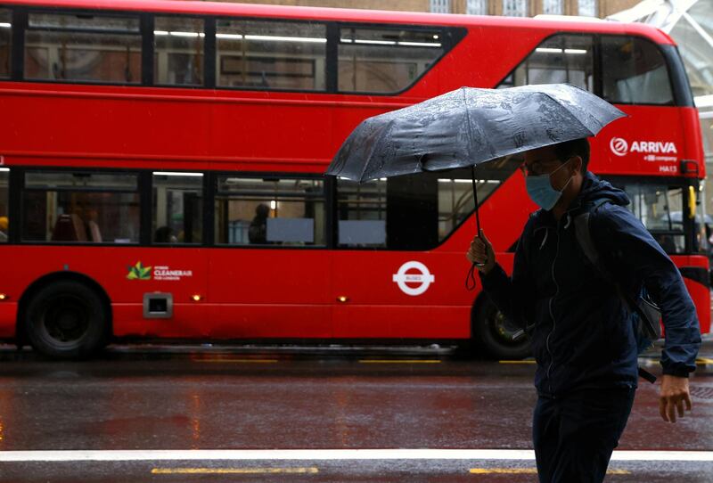A man with an umbrella walks past a bus in the City of London financial district during the morning rush hour in London, Britain September 25, 2020. REUTERS/John Sibley