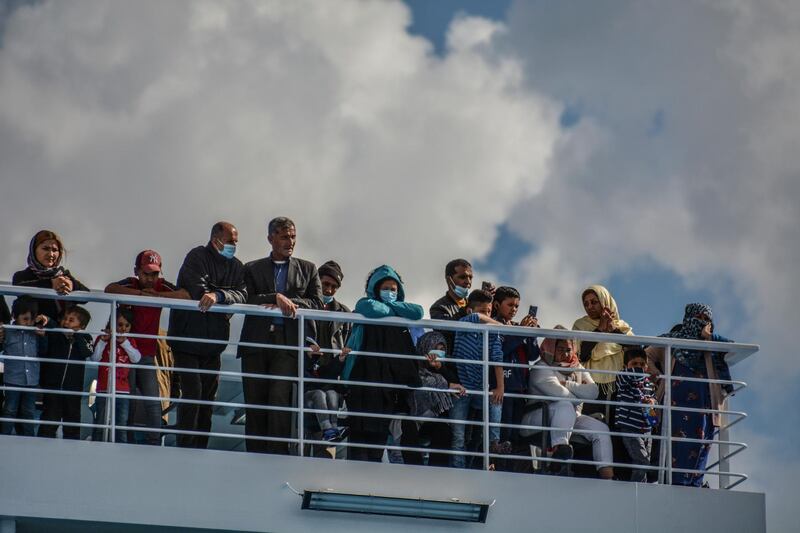 Migrants stand on a deck of a ship bound for Piraeus at the port of Mytilene, on the northeastern Aegean island of Lesbos, Greece, on Sunday, May 3, 2020. Greek authorities are moving 400 migrants, mostly families, to the mainland to help ease overcrowded conditions at the camp. The migrants will arrive in the port of Piraeus on two passenger ships Monday morning. (AP Photo/Panagiotis Balaskas)