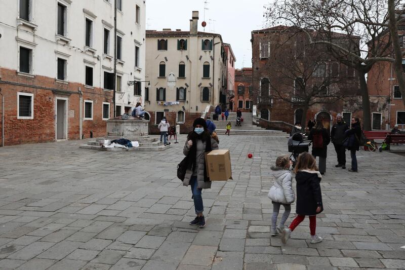 A Venetian wearing a protective mask walks by children playing in a square on in Venice, Italy. Getty Images