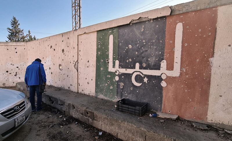 (FILES) In this file photo taken on November 19, 2020, a Libyan stands in front of a school, which was damaged during fighting between rival factions, in the capital Tripoli's suburb of Ain Zara. The writing on the wall reads "Libya" in Arabic.  Foreign forces ignored a deadline to pull out of Libya as scheduled Saturday under a UN-backed ceasefire deal, highlighting the fragility of peace efforts after a decade of conflict. / AFP / Mahmud TURKIA
