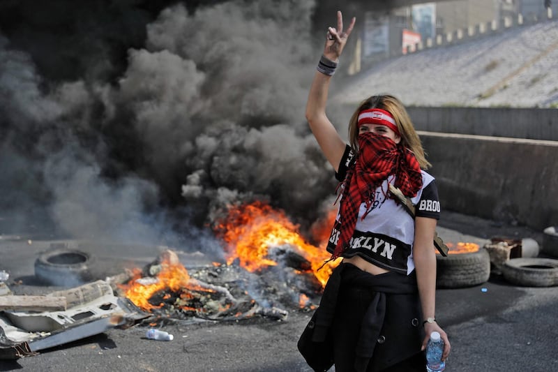 A bandana-clad anti-government demonstrator gestures as she stands by the smoke of burning tires at a makeshift roadblock in Zouk Mosbeh, north of Lebanon's capital Beirut. AFP