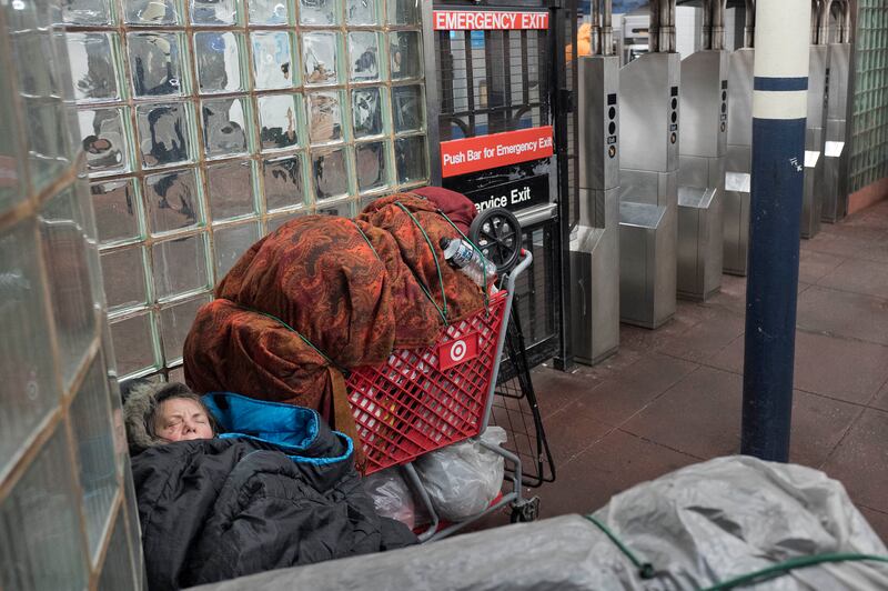 A homeless person sleeps next to a shopping trolley of belongings in a New York subway station. AP