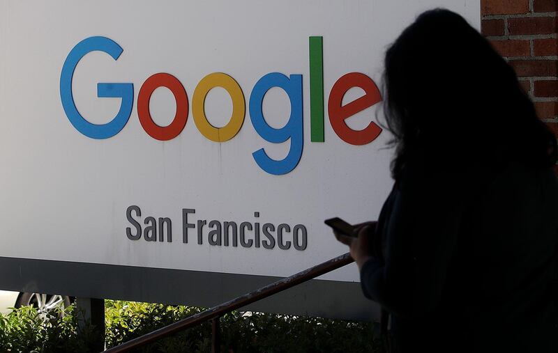 FILE - In this May 1, 2019, file photo, a woman walks past a Google sign in San Francisco. The U.S. Justice Department and the Federal Trade Commission are moving to investigate Google, Facebook, Amazon and Apple over their aggressive business practices, and the House Judiciary Committee has announced an antitrust probe of unidentified technology companies. (AP Photo/Jeff Chiu, File)