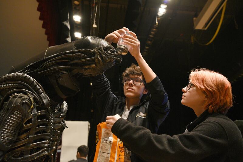 FILE - In this March 25, 2019 file photo, North Bergen High School's Xavier Perez, 16, the Alien, is covered in slime by his handlers Eddie Mantilla, 15, and Cassandra Klima, 16, as they work on the play "Alien," an adaptation of the Ridley Scott movie, in North Bergen, N.J. The New Jersey high school's stage production of "Alien" is coming back with help from the 1979 film's director, Ridley Scott, after his production company provided $5,000 so the school could put on an encore performance April 26. On Friday, April 26, 2019, Sigourney Weaver was at the school to watch the encore performance herself, telling the crowd before the curtain rose that â€œthis is the night Iâ€™ve been waiting for.â€ (Amy Newman/The Record via AP)