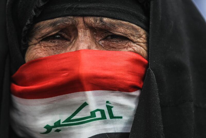 An elderly Iraqi woman, her face covered with a national flag, cries as she watches anti-government demonstrators protesting in the capital Baghdad's Tahrir square. AFP