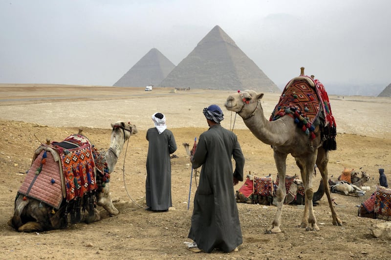 A picture taken on February 15, 2018 shows Egyptian tour guides preparing a caravan of camels for tourists as they sit across the Giza plateau from (R to L) the Great Pyramid of Khufu (Cheops), the Pyramid of Khafre (Chephren), and the Pyramid of Menkaure, on the southwestern outskirts of the capital Cairo. / AFP PHOTO / MARIO GOLDMAN