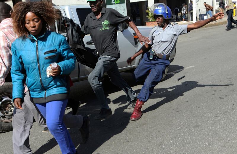 A riot police man kicks out at a man during protests. AP Photo