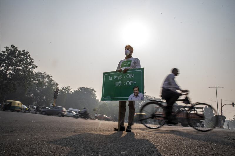 A cyclist rides past a worker holding a sign, requesting motorists to turn off their engines while waiting at a traffic signal, in New Delhi. Bloomberg