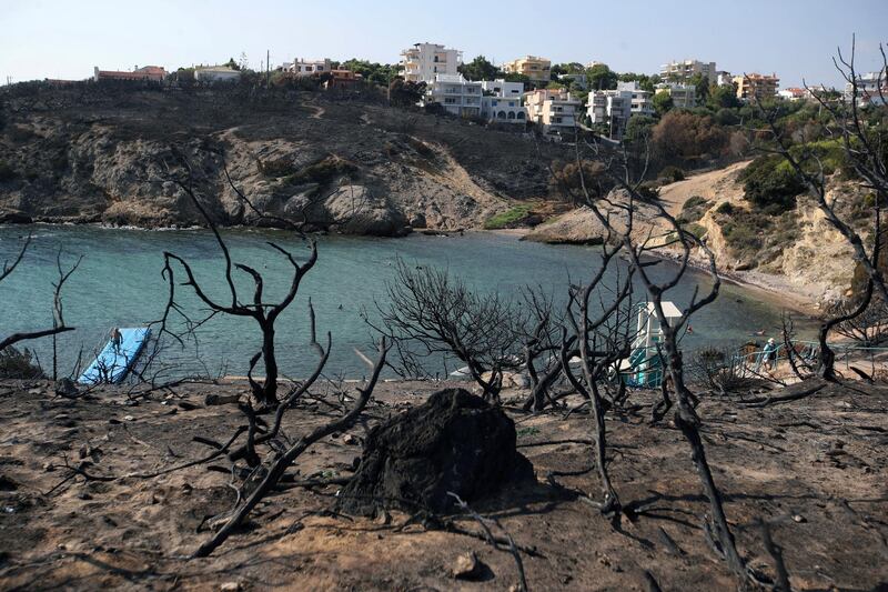 FILE In this Wednesday, Aug. 1, 2018 file photo people swim at a beach in Rafina, east of Athens, ten days after the Greece's deadliest wildfire in decades that killed 100 people. Three migrant fishermen have been awarded Greek citizenship after rescuing scores of people forced into the sea by a major wildfire outside Athens that left 100 people dead last summer. Greek President Prokopis Pavlopoulos hosted the ceremony Wednesday, Jan. 2, 2019 for Gani Xheka from Albania and Egyptians Emad El Khaimi and Mahmoud Ibrahim Musa. (AP Photo/Thanassis Stavrakis, file)