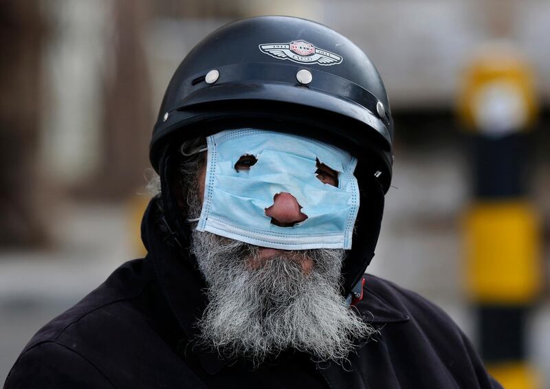 A man with a motorcycle helmet covers his face with a mask, as he watches municipal policemen order people to leave the corniche, or waterfront promenade, along the Mediterranean Sea, as the country's top security council and the government were meeting over the spread of coronavirus, in Beirut, Lebanon.  AP Photo