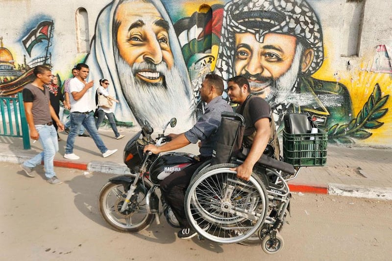 Moamen Qreiqea holds his wheelchair as he rides on a motorcycle past murals of late leader Yasser Arafat and late Hamas spiritual leader Ahmed Yassin, on a street in Gaza City.