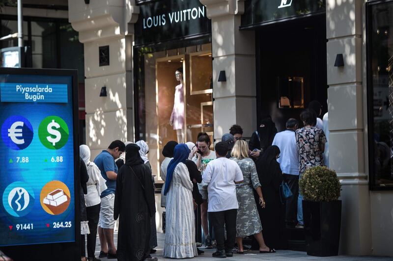 Tourists, many from Saudi Arabia and Asia, stand in a queue outside a luxury brand Louis Vuitton store next to a digital billboard giving updates on various currencies and the Turkish stock exchange in Istanbul on August 13, 2018. - Turkey's troubled lira tumbled on August 13 to fresh record lows against the euro and dollar, piling pressure on stock markets on fears the country's crisis could spill over into the world economy. (Photo by Yasin AKGUL / AFP)