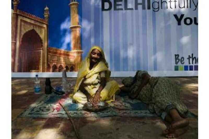 Homeless women sit in front of a Commonwealth Games sign. The government has been seeking to send migrants to their home states. Manpreet Romana / AFP