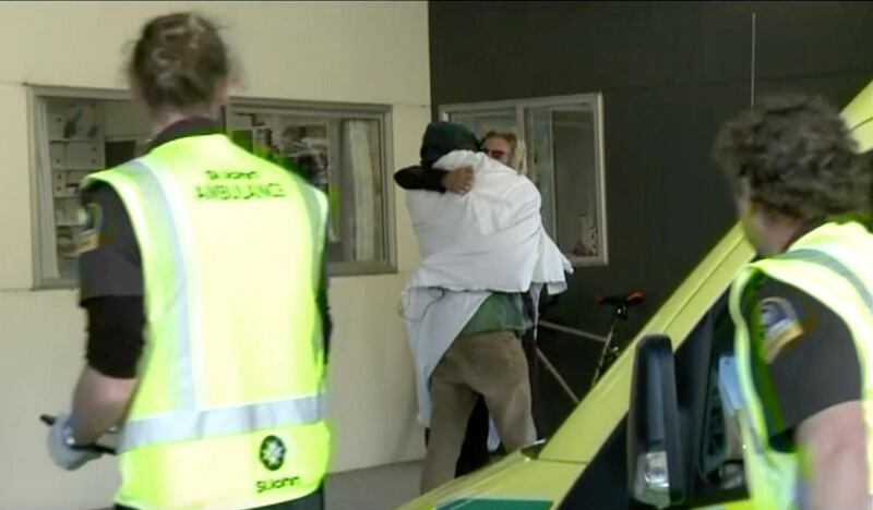 In this image made from May 27, 2020, video, one of the two hikers found alive is wrapped in a white blanket hugs another person as they enter a hospital in Nelson, New Zealand. Two hikers rescued in the New Zealand wilderness Wednesday got lost in fog and exhausted their food but survived 19 days with only minor injuries, police said. (Newshub/TVNZ via AP)