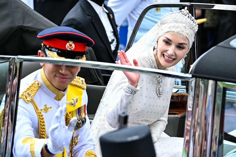 Prince Abdul Mateen and Yang Mulia Anisha Rosnah wave from their car during the wedding procession in Brunei's capital Bandar Seri Begawan on January 14, 2024.  (Photo by MOHD RASFAN  /  AFP)
