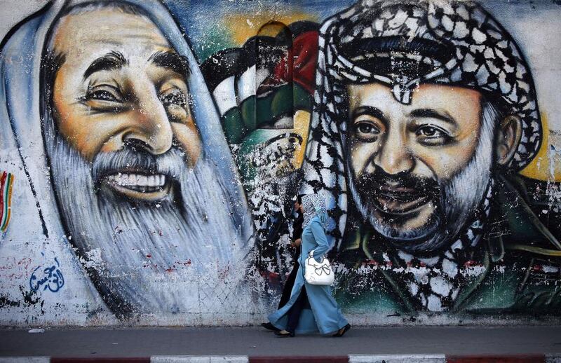 Palestinian women walk past a mural depicting late Hamas spiritual leader Sheikh Ahmed Yassin, left, and late Palestinian leader Yasser Arafat in Gaza City. Thomas Coex / AFP