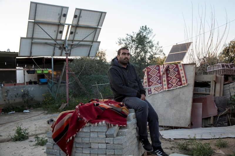 Mohamed Abu Queder ,35, sits on a pile of cement construction blocks and traditional carpets and solar panels  in the unrecognised village of Al-Zarnoug near the southern Israeli city of Beersheba. Unrecognised  illegal villages like this one have  scarce access to water, electricity and other services. (Photo by Heidi Levine for The National).