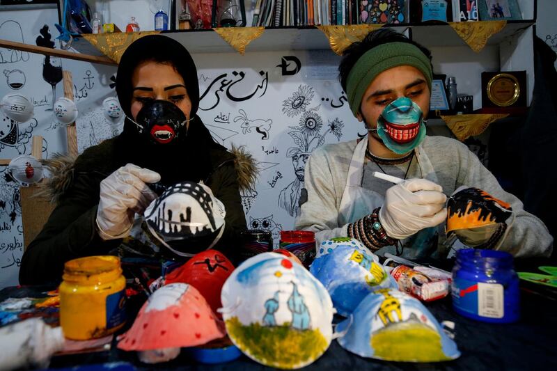 Palestinian artists Samah Said (L) and Dorgham Krakeh (R) paint masks for a project raising awareness about the COVID-19 coronavirus pandemic, in Gaza City.   AFP