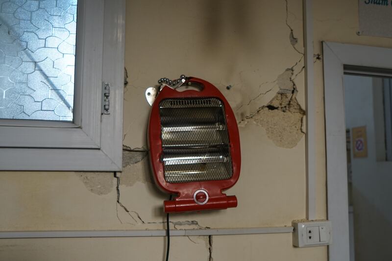 An electric heater hangs from a cracked wall