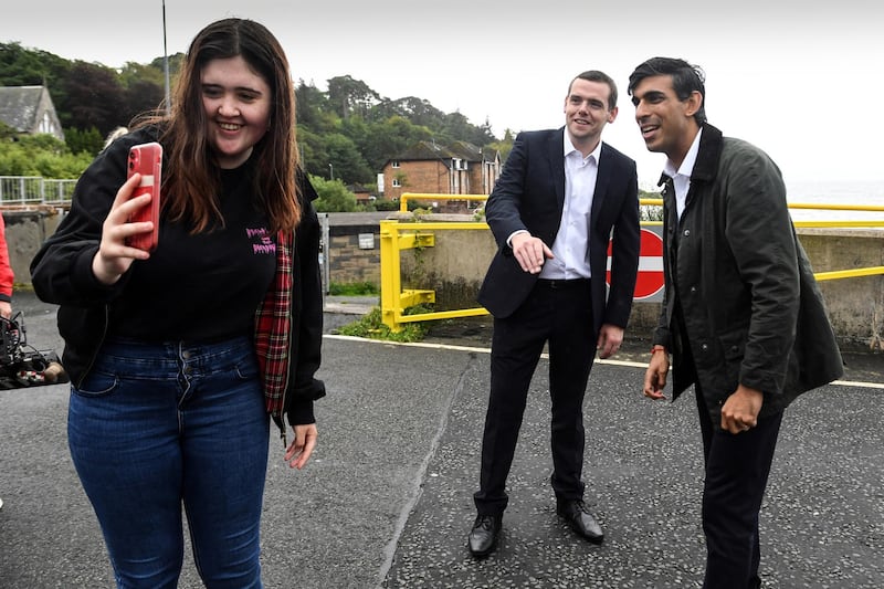 A member of the public takes a selfie photograph with Britain's Chancellor of the Exchequer Rishi Sunak (R) and Douglas Ross (C), the new Leader of the Scottish Conservative Party at Wemyss Bay on the west coast of Scotland on August 7, 2020. (Photo by Andy Buchanan / AFP)