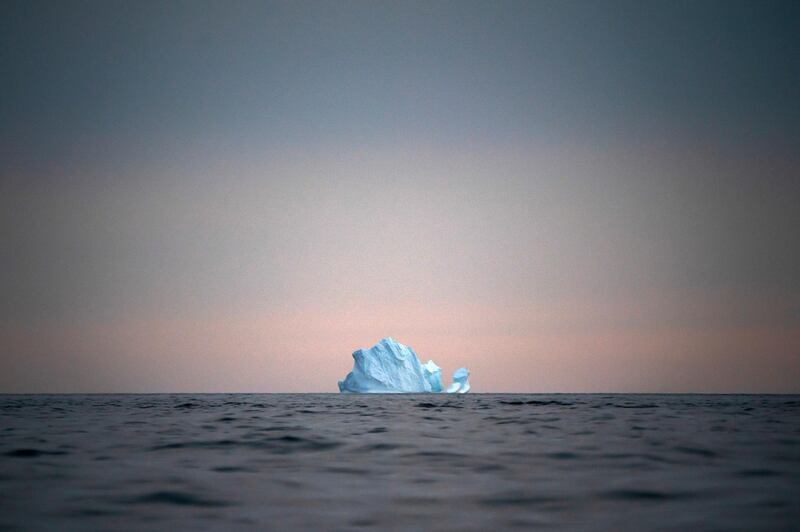 A large Iceberg floats away as the sun sets.