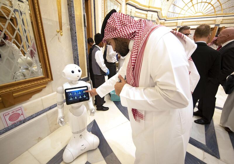 An attendee finds out event information on a tablet carried by a robot on the opening day of the Future Investment Initiative (FII) forum at the Ritz Carlton hotel in Riyadh, Saudi Arabia, on Tuesday, Oct. 29, 2019. Central banks have run out of firepower to fight the next economic downturn, according to global finance chiefs gathered at an investment forum in Saudi Arabia on Tuesday. Photographer: Faisal Al Nasser/Bloomberg