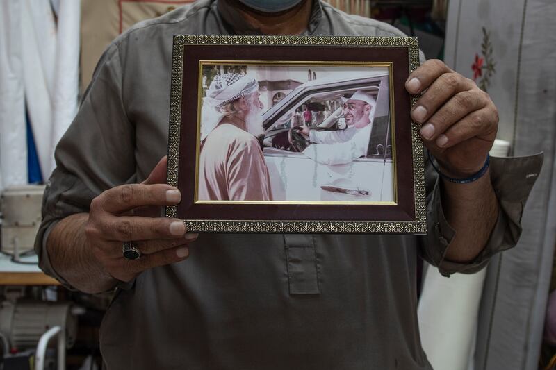 Muhammed holds a photo of his father meeting Sheikh Mohammed bin Zayed, Vice President and Ruler of Dubai, in 2018. The image takes pride of place in his shop.