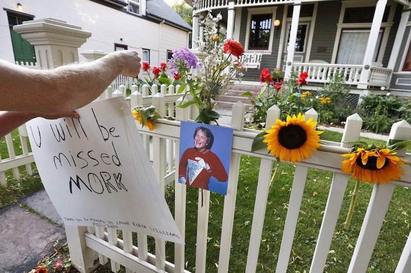 A man hangs a placard alongside flowers and a photo of the late actor Robin Williams as Mork from Ork, as people pay their respects at the home where the 80's TV series Mork & Mindy, starring Williams, was set, in Boulder, Colombo, Monday August 11, 2014. AP