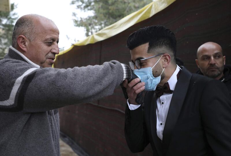 Palestinian groom Imad Sharaf (R), wearing gloves and a face mask, kisses his father's hand as part of tradition upon arriving home in the village of al-Dahriya, south of Hebron in the West Bank.  AFP