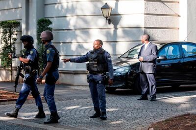 An armed South African Police member gestures as he leaves with colleagues the compound of the controversial business family Gupta while cars belonging to the Hawks, The Directorate for Priority Crime Investigation, are stationed outside, in Johannesburg, on February 14, 2018.
South African police on February 14 raided the Johannesburg house of the Gupta family, which is accused of playing a central role in alleged corruption under scandal-tainted President Jacob Zuma. Zuma has been ordered to resign by the ruling ANC party, and is expected to respond to the order later on February 14. / AFP PHOTO / WIKUS DE WET