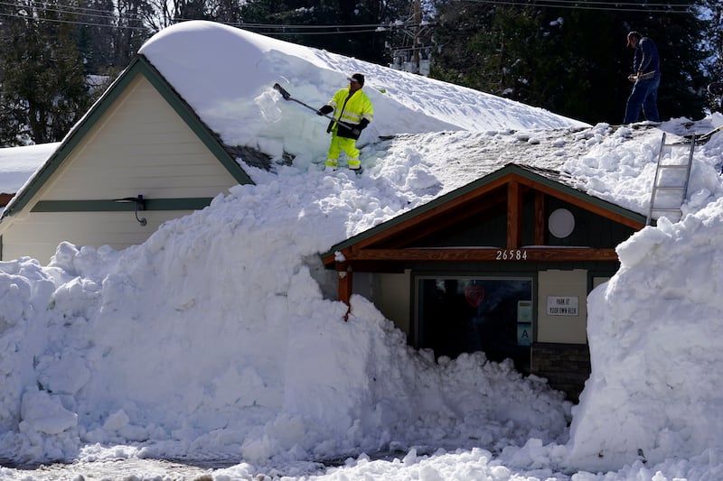 A worker clears snow off the roof of Skyforest Elks Lodge after a series of winter storms, in Rimforest, California. AP