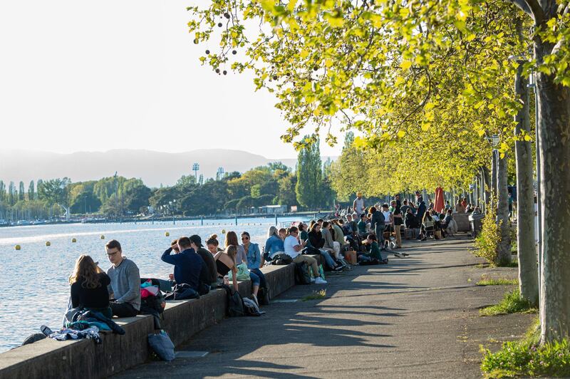People sit by the banks of Lake Geneva in Lausanne. Switzerland has eased lockdown restrictions with measures that include allowing restaurants, cinemas, theatres and zoos to reopen. Getty Images