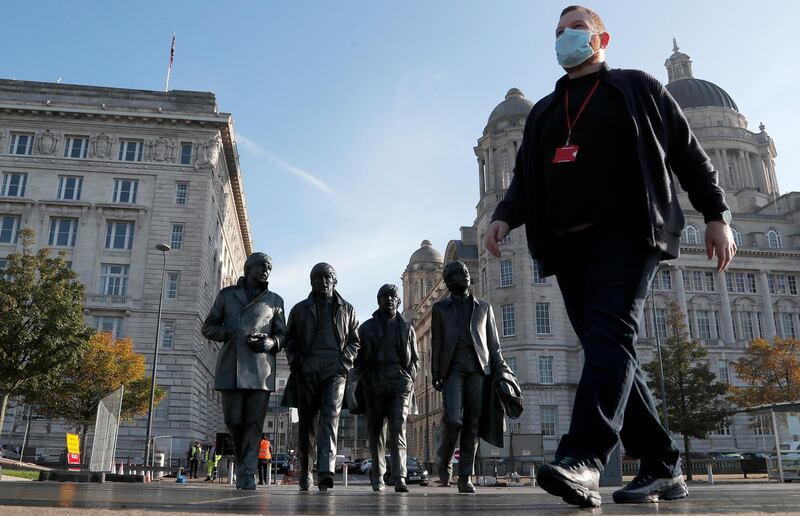 A man wearing a face mask walks past a statue of the Beatles, as new measures across the region are set to come into force in Liverpool. AP Photo