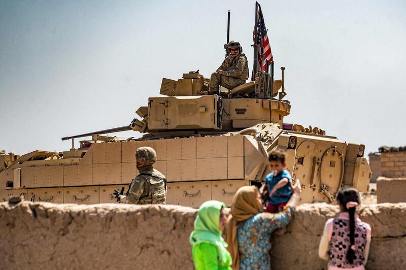 Women and a child in Rmelan, with a US Bradley Fighting Vehicle on patrol in the background. AFP