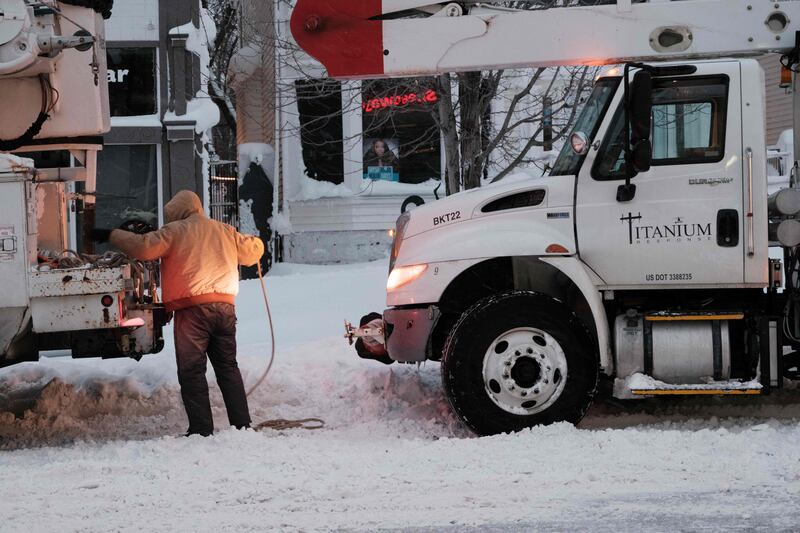 A utility worker straps a rope to a truck to try to tow it out of a snowdrift. AFP