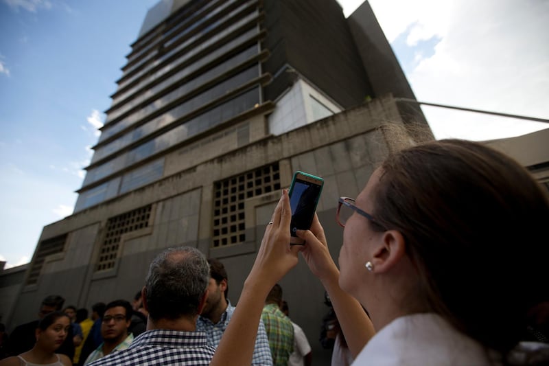 Manuela Bolivar, a lawmaker and member of the First Justice party, takes photos of the Bolivarian National Security Service (SEBIN) headquarters in Caracas, Venezuela, Monday, Oct. 8, 2018. Venezuela's Attorney General Tarek William Saab said Monday that councilman Fernando Alberto Alban Salazar, who was arrested on suspicion of involvement in a failed assassination attempt on President Nicolas Maduro, has died of suicide while jailed at SEBIN. (AP Photo/Fernando Llano)